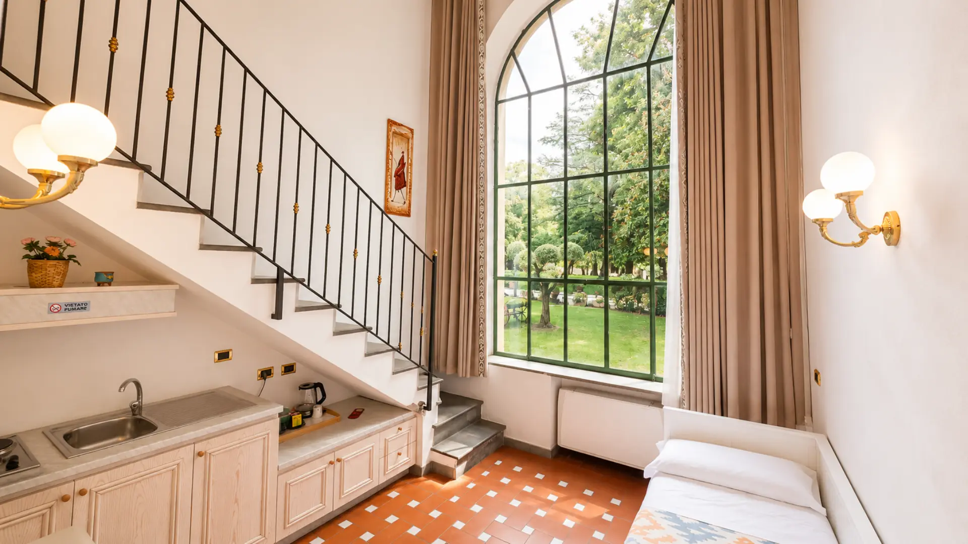 Un loft su due piani: la scala che sale al soppalco, l'angolo cottura e la vetrata alta sul parco