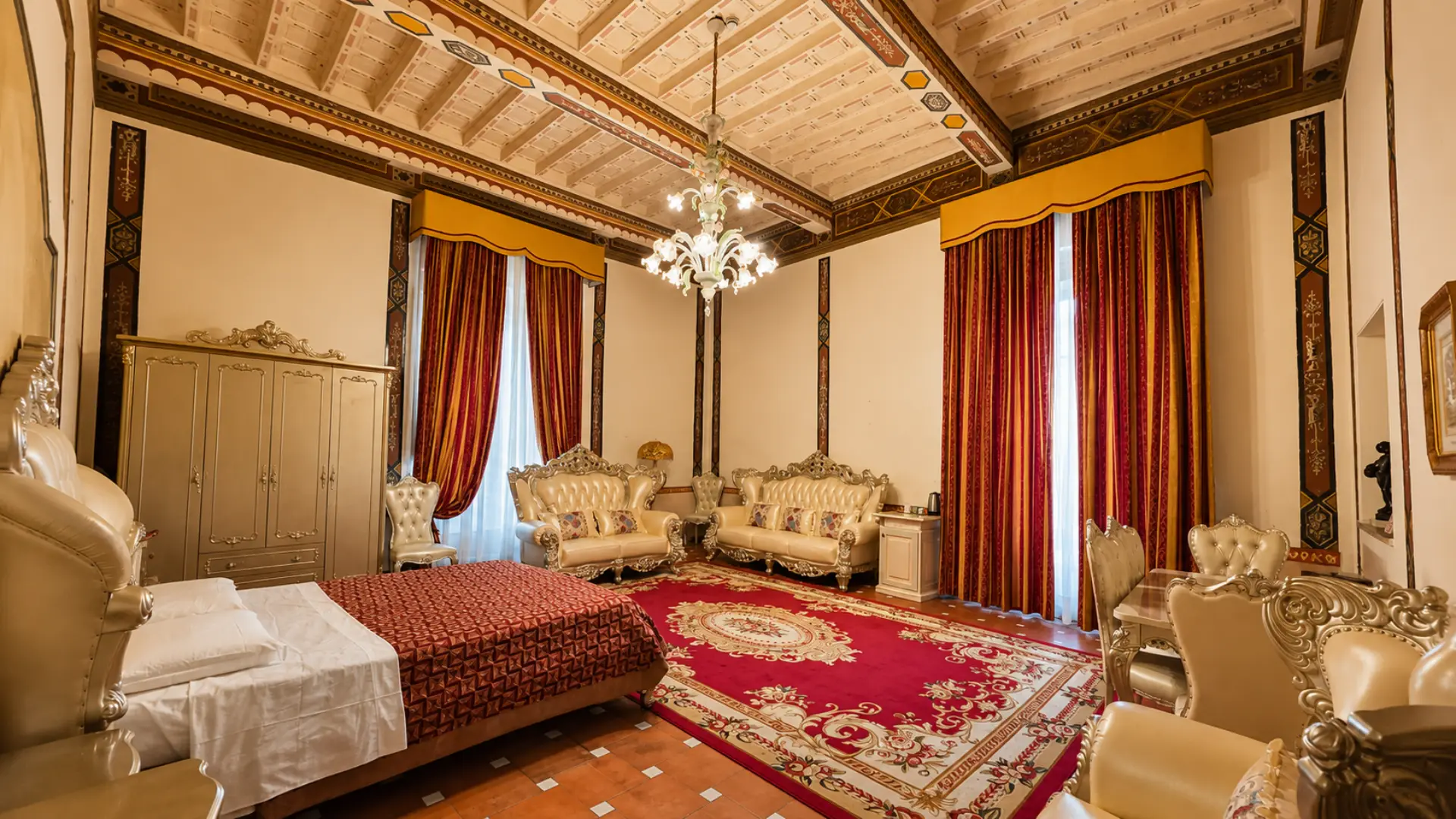 Una camera della villa: il soffitto a cassettoni dipinto, il lampadario in vetro, le tende rosse e il tappeto sul pavimento in cotto